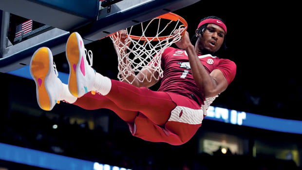Arkansas guard Ricky Council looks down over Auburn defenders while his feet touch the backboard on a dunk.